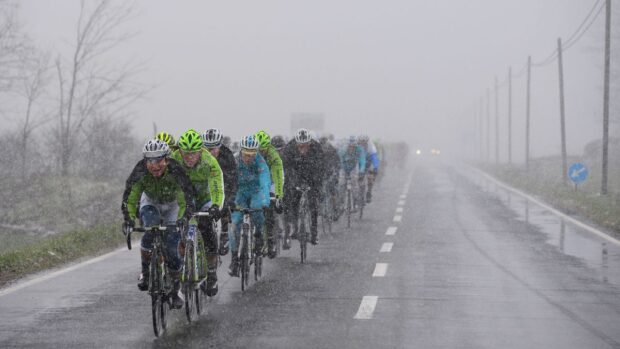 A peloton riding single file along a snowy road in poor conditions