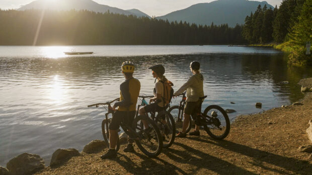 A family with mountain bikes pauses by lakeshore at sunset