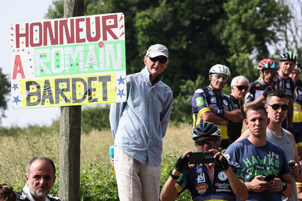 Spectators stand on the side of the road next to a placard reading "honor to Romain Bardet during the 3rd stage of the 77th edition of the Criterium du Dauphine cycling race, 207,2 km between Brioude and Charantonnay, on June 10, 2025. (Photo by Anne-Christine POUJOULAT / AFP)