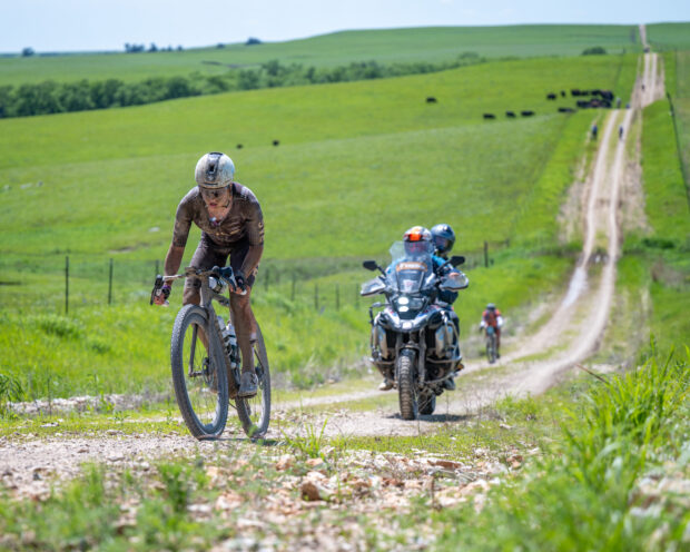 A Life Time media motorbike trails a PAS Racing rider at Unbound Gravel 200