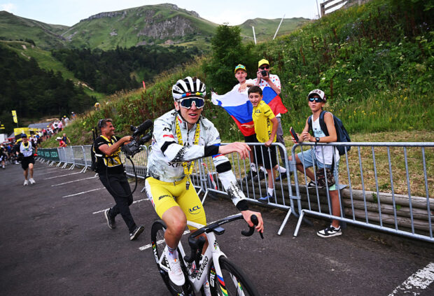 Tadej Pogacar heads back to the team bus after stage 10 of the Tour de France, wearing a white jacket over his yellow skinsuit.
