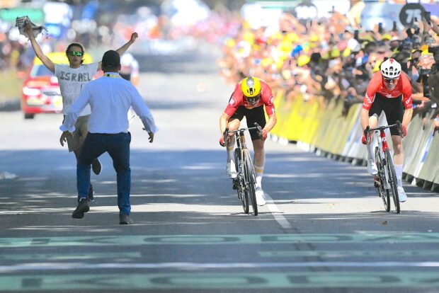 A Tour de France staff member attempts to intercept an individual running at the finish line area as Uno-X Mobility team's Norwegian rider Jonas Abrahamsen (C) cycles ahead of Team Jayco AlUla team's Swiss rider Mauro Schmid (R) to the finish line to win the 11th stage of the 112th edition of the Tour de France cycling race, 156.8 km starting and finishing in Toulouse, southwestern France, on July 16, 2025. (Photo by Marco BERTORELLO / AFP) (Photo by MARCO BERTORELLO/AFP via Getty Images)