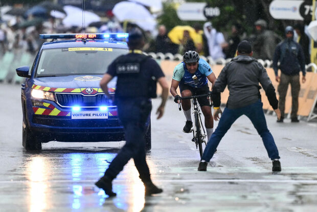 A French Republican Security Corps (CRS - Compagnies Republicaines de Securite) officer and a Tour de France staff member prepare to intercept an individual attempting to cycle across the finish line minutes before the final sprint of the 112th edition of the Tour de France cycling race, 160.4 km between Bollene and Valence, southern France, on July 23, 2025. (Photo by Marco BERTORELLO / AFP)