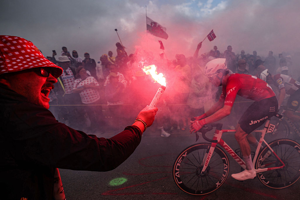 A spectator waves a flare as Team Jayco AlUla team's Swiss rider Mauro Schmid cycles in an ascent in the final kilometres of the 2nd stage of the 112th edition of the Tour de France cycling race, 209.1 km between Lauwin-Planque and Boulogne-sur-Mer, Northern France, on July 6, 2025. (Photo by Anne-Christine POUJOULAT / AFP) (Photo by ANNE-CHRISTINE POUJOULAT/AFP via Getty Images)