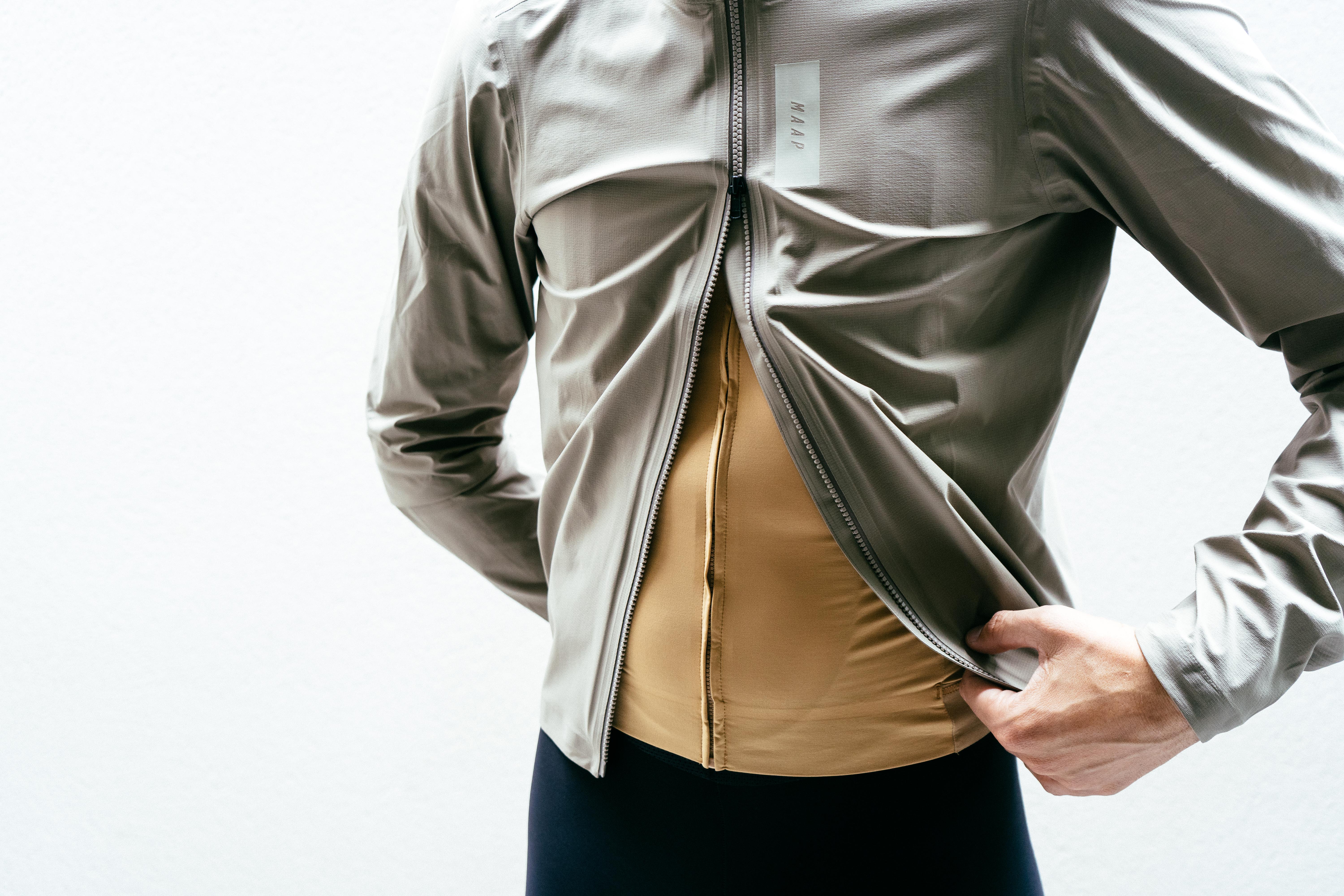 Una chaqueta ciclista impermeable de color blanco roto con la cremallera desabrochada desde abajo