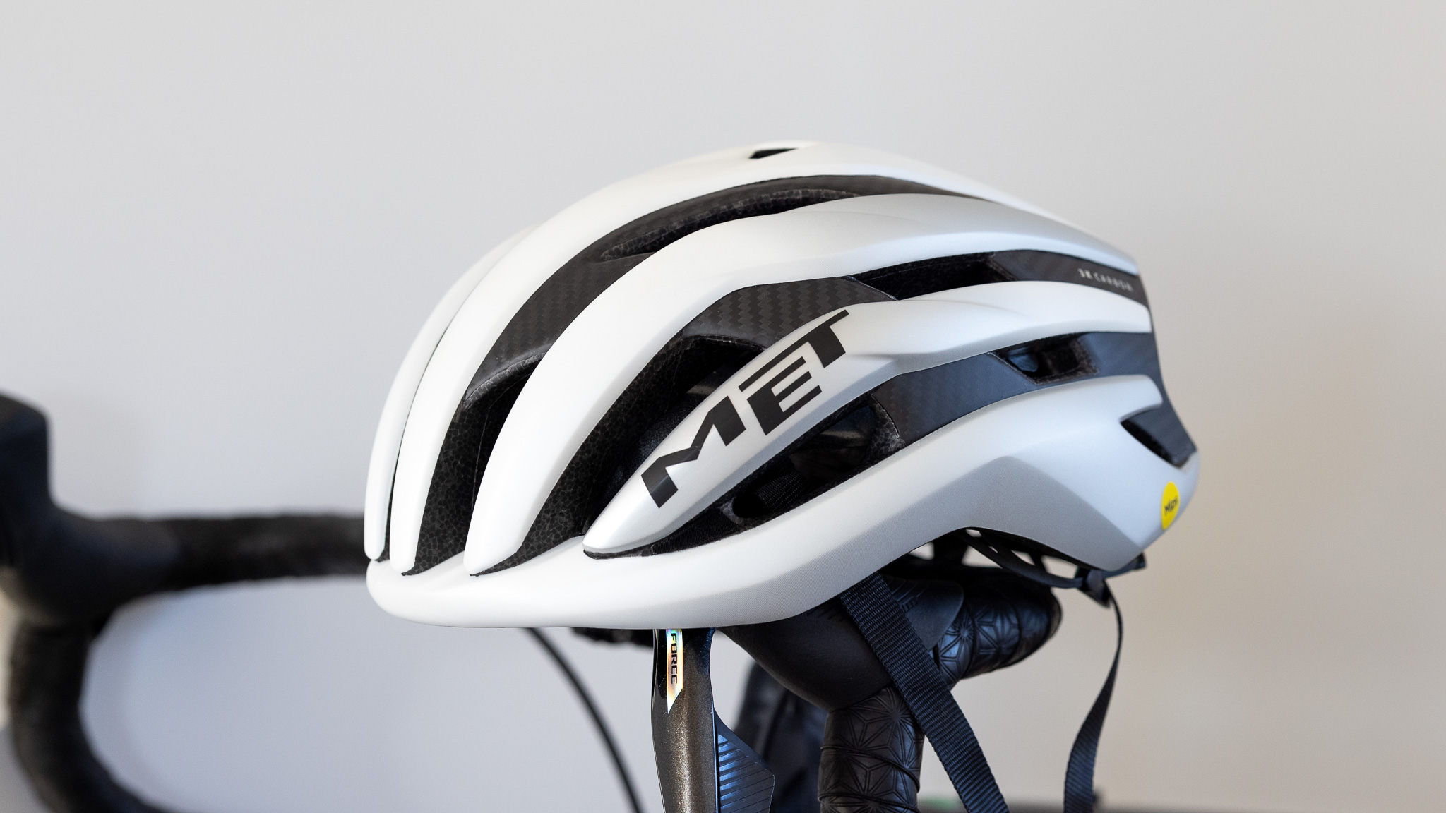 El casco MET Trenta 3K Carbon MIPS en blanco en el manillar de la bicicleta detalles en primer plano
