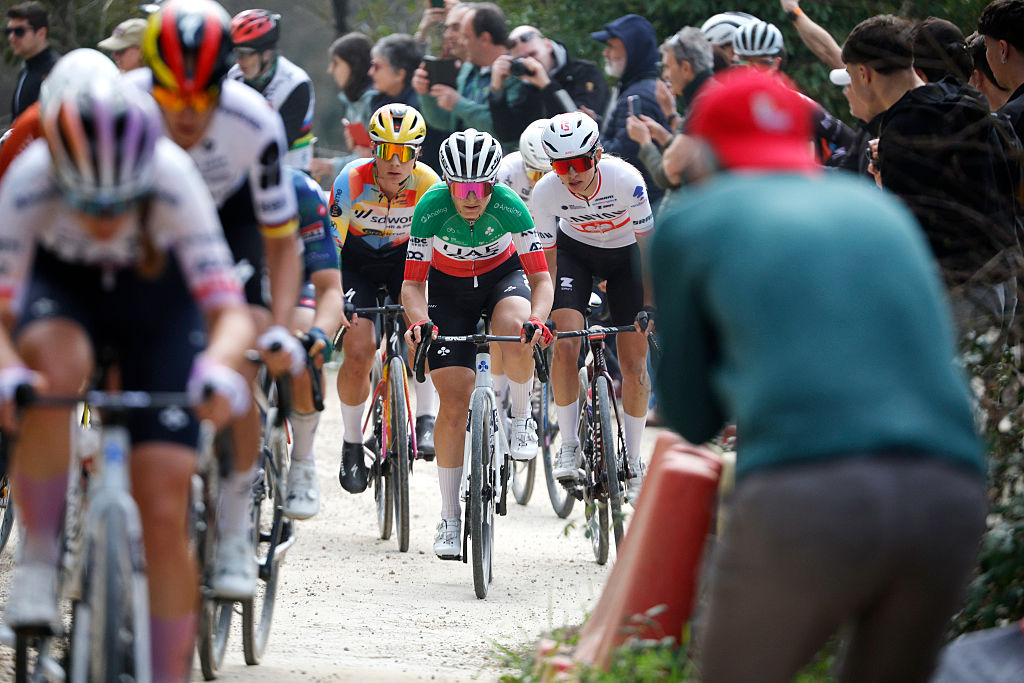 Una toma larga, tomada en Strade Bianche Women 2026, que muestra a las corredoras borrosas en primer plano y luego se enfoca en Elisa Longo Borghini, Lotte Kopecky y Kasia Niewiadoma-Phinney detrás.