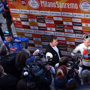 A wide view of the mixed zone with Pogacar in front of the Milan-San Remo sponsor backdrop. Jasper Philipsen and Mathieu van der Poel are being interviewed to his left