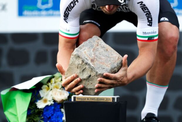 A rider stoops to pick up the cobblestone trophy as Paris-Roubaix winner