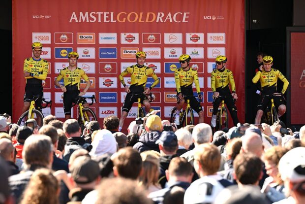 A wide, far away shot of Visma-Lease a Bike riders on the podium for sign on at the start of Amstel Gold Race men's 2026, with the crowd in the foreground