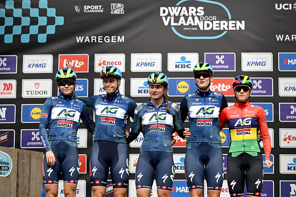 Una foto de cinco corredores de AG Insurance-Soudal parados en el escenario, uno al lado del otro, en el cartel de la presentación antes de Dwars Door Vlaanderen 2026.