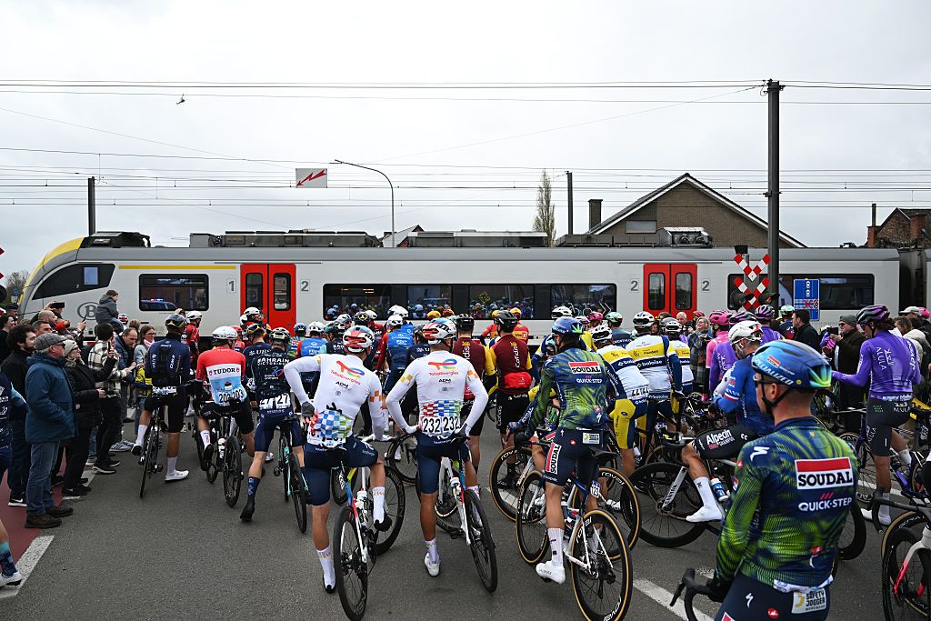 Riders wait at a level crossing for a train to pass during the 2026 Tour of Flanders