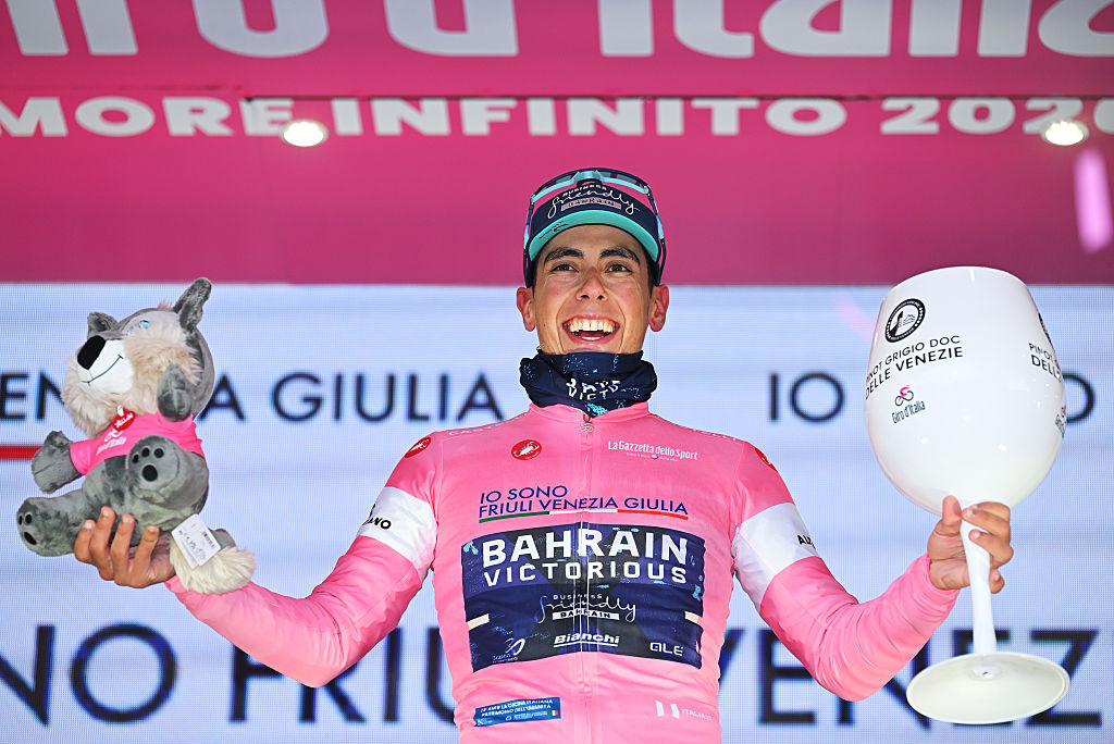 Afonso Eulalio luciendo la maglia rosa en el podio, con una copa de vino enorme y peluda como premio en cada mano