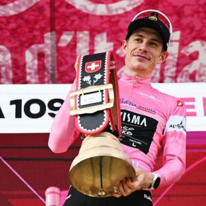 Jonas Vingegaard in the pink jersey on the podium holds a huge bell as prize by the Swiss hosts