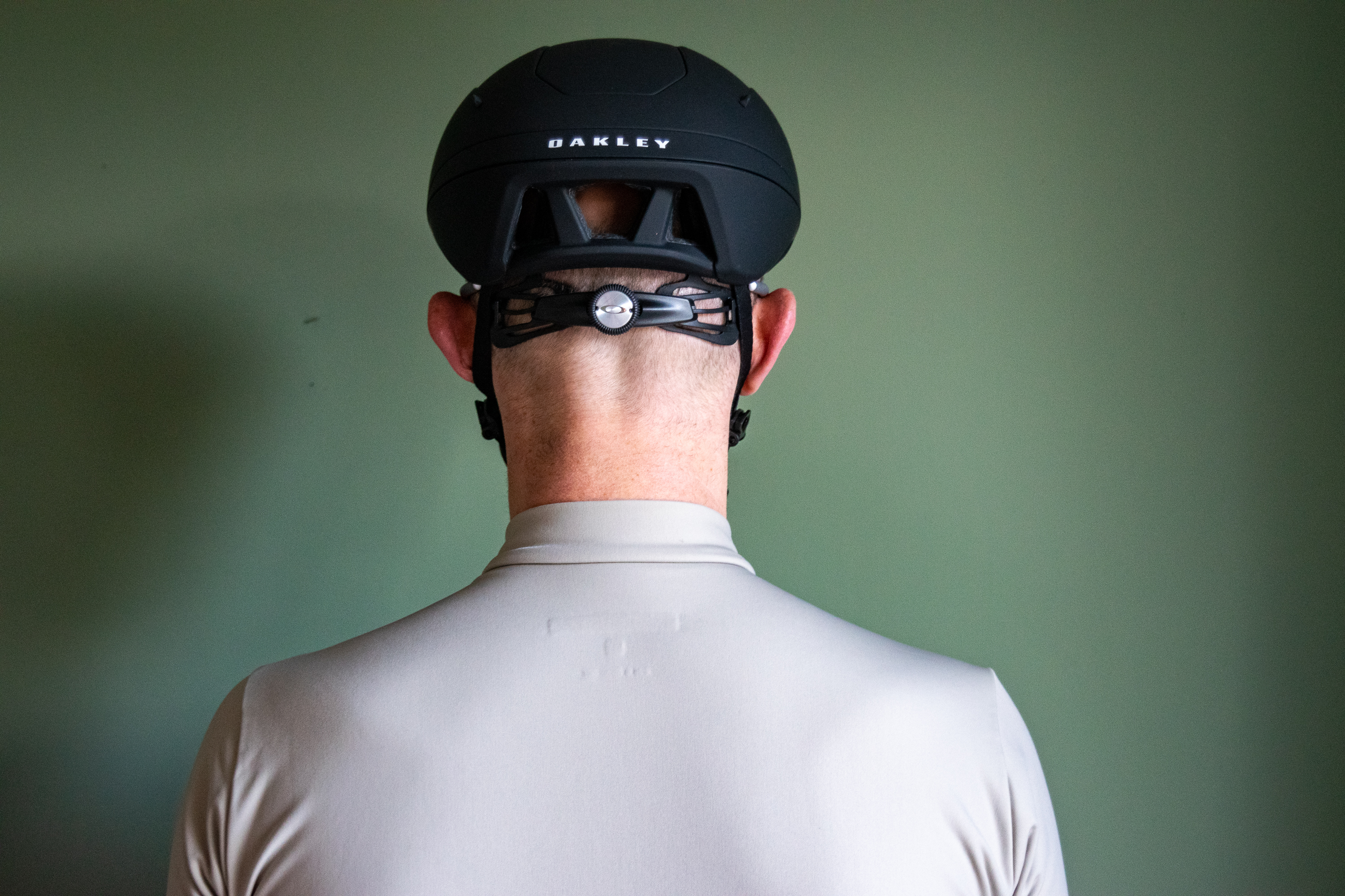 Un ciclista con un casco Oakley Velo Mac negro frente a una pared verde