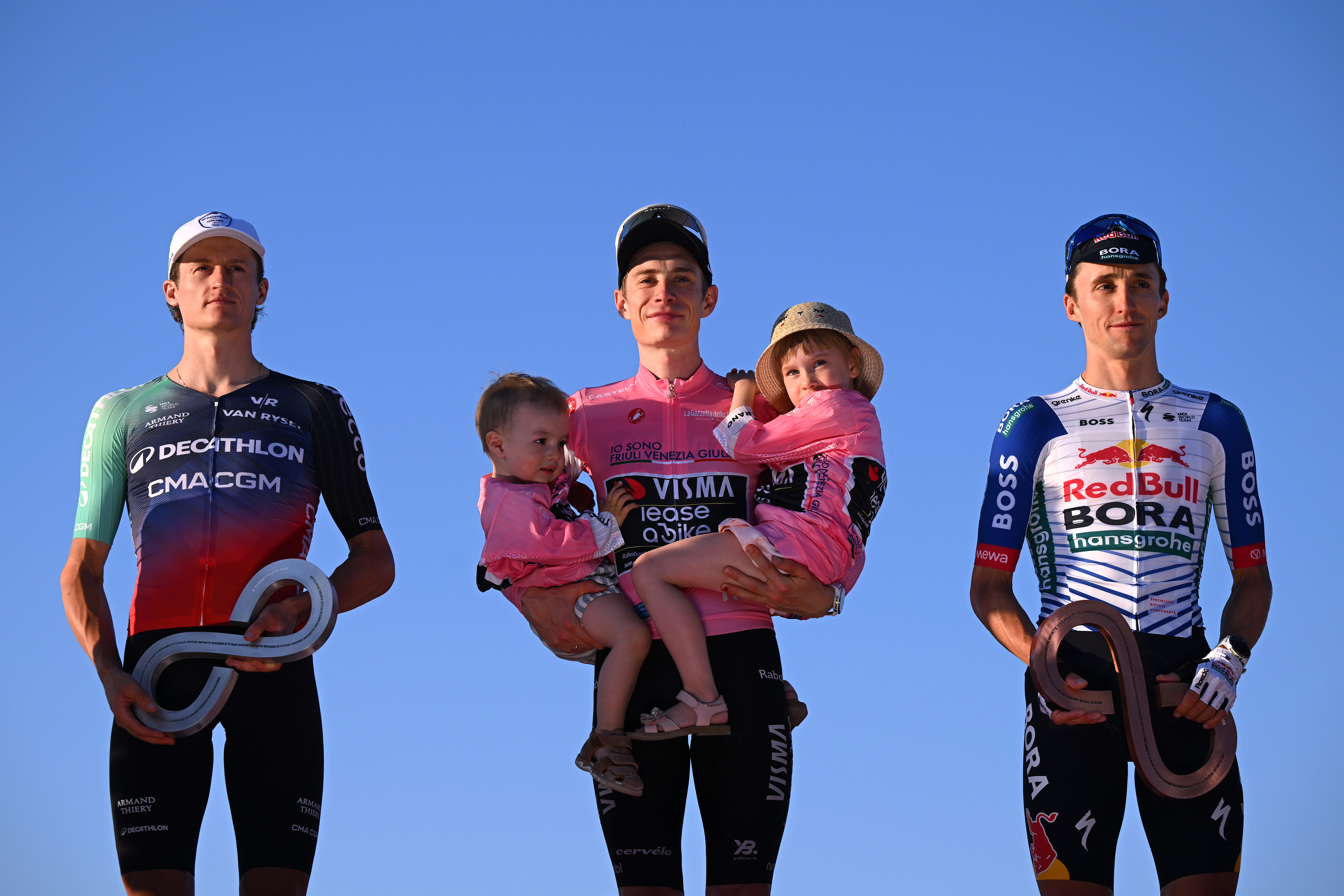Gall, Vingegaard con sus hijos en brazos y Hindley en el podio contra un cielo azul