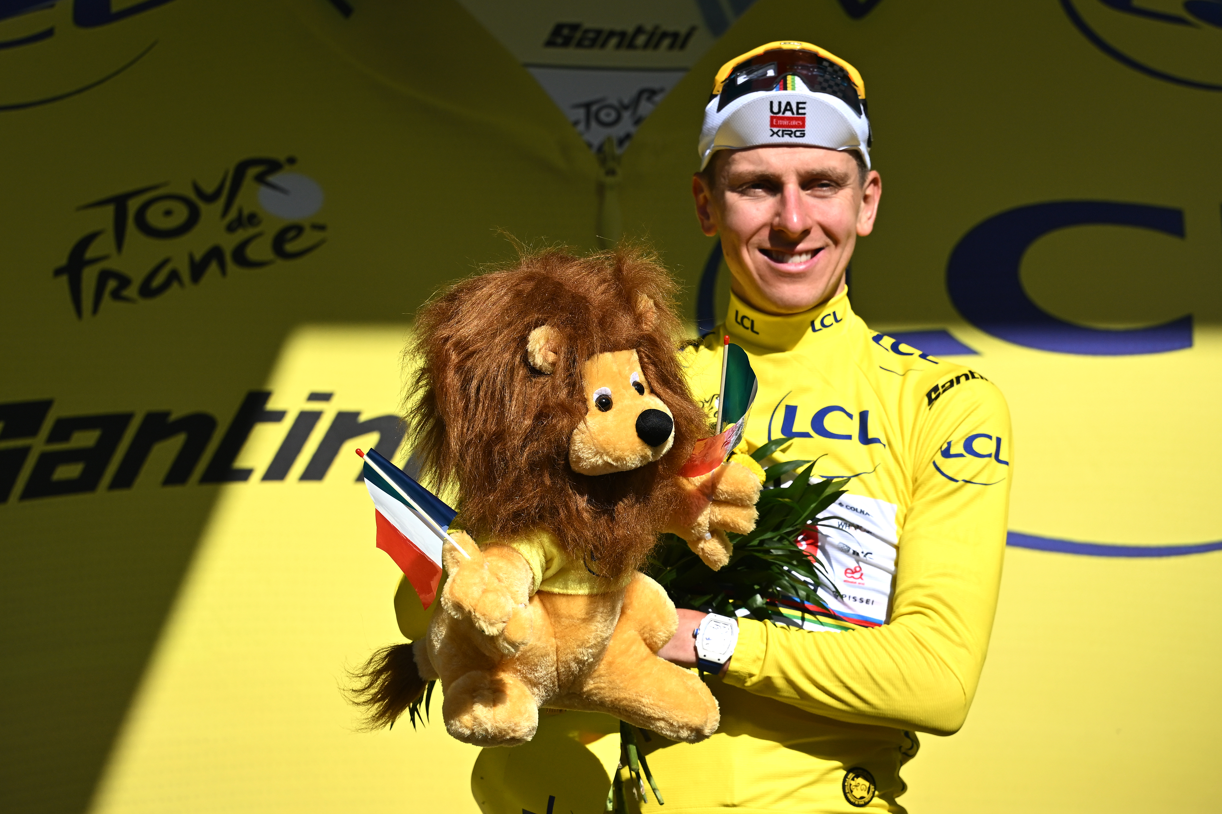 Tadej Pogačar viste el maillot amarillo y sostiene un león de juguete en el podio del Tour de Francia