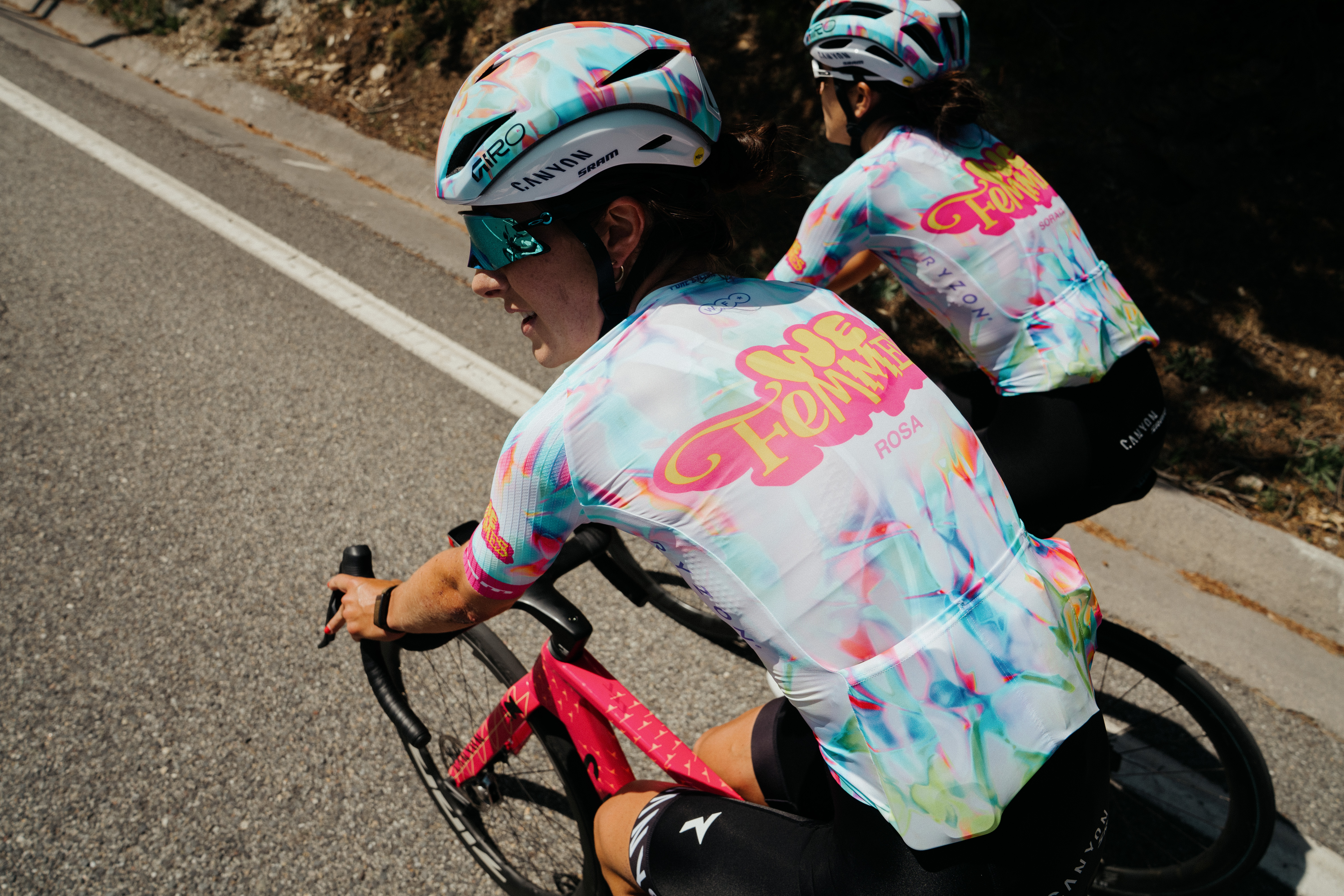 Nuevo kit Canyon-SRAM, que presenta un fondo blanco claro con detalles coloridos en rosa, azul, naranja y verde, además de un kit 'We Femmes' rosa y amarillo. logo