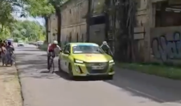 Screen grab of video showing two riders holding onto side of team car at Tour de Guadeloupe