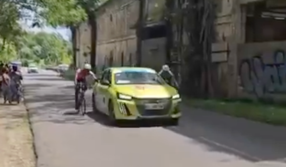 Screen grab of video showing two riders holding onto side of team car at Tour de Guadeloupe