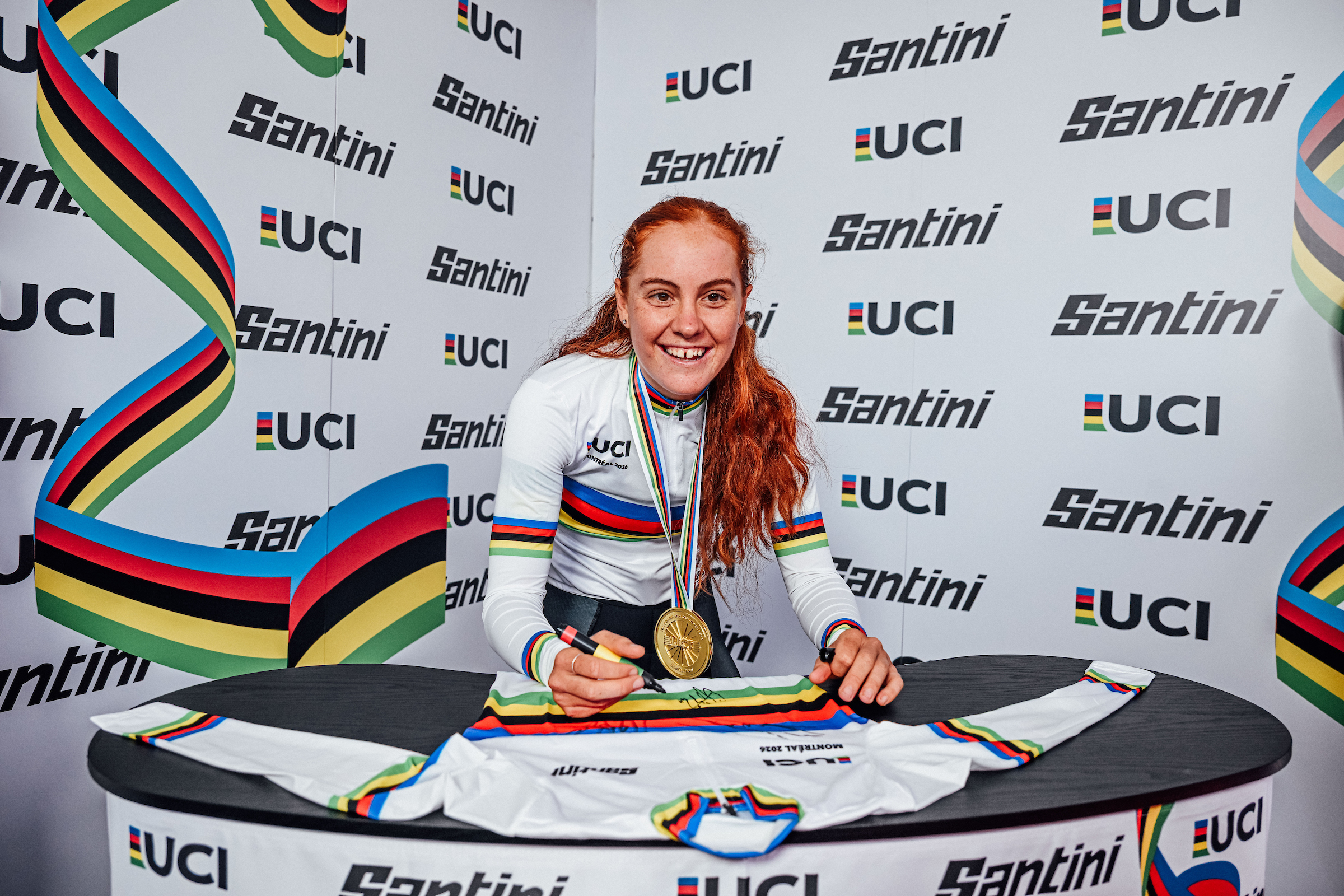 Felicity Wilson-Haffenden sonríe y firma una camiseta tras ganar la contrarreloj femenina sub-23 del Mundial de Ruta 2026